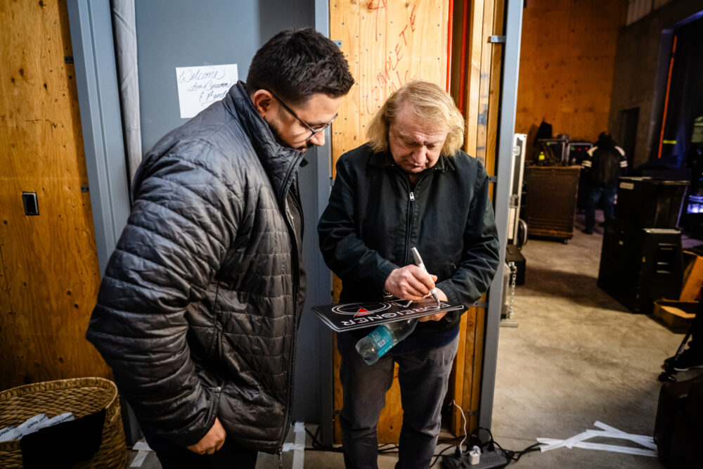 Man signing skateboard while another man watches
